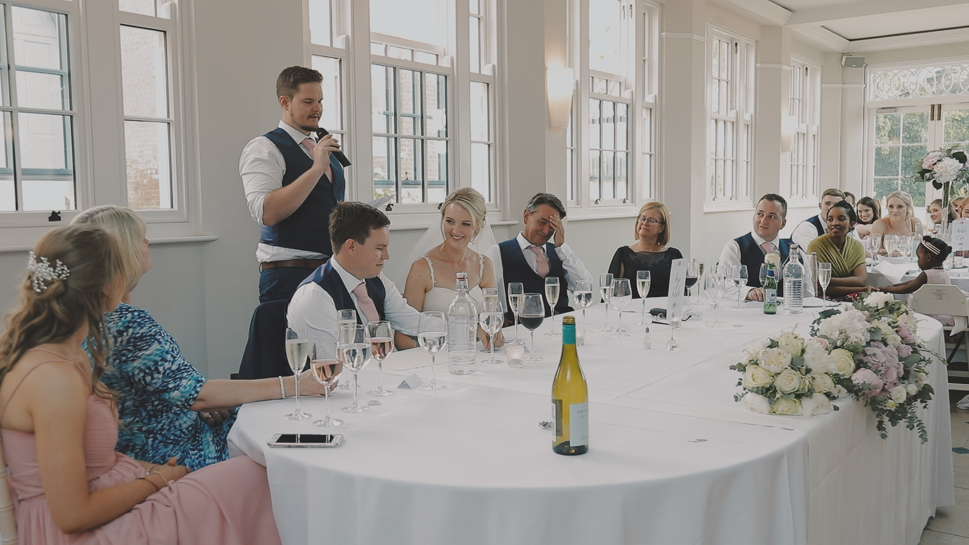 Wedding reception speech at Rockbeare Manor in Devon inside the ballroom with bride and groom seated at a flower-decorated top table