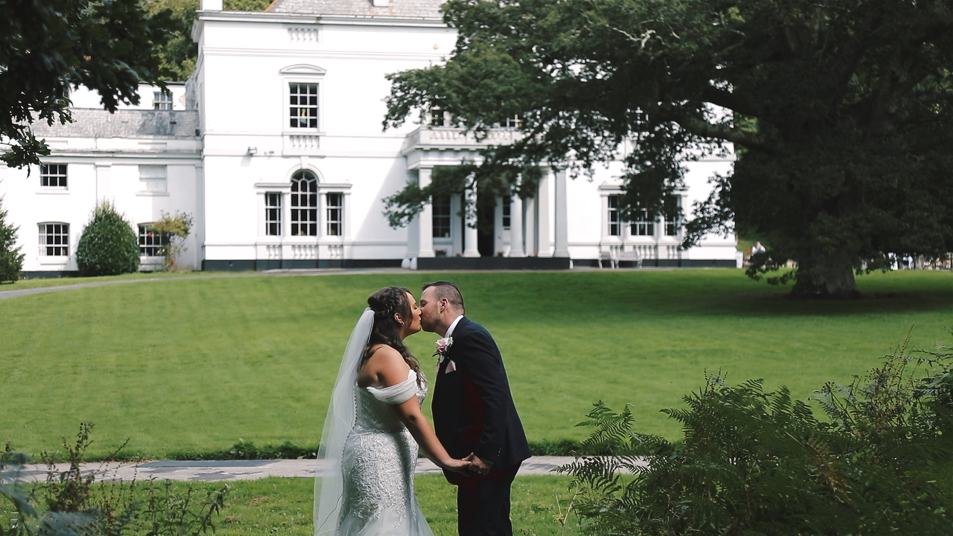 Wedding couple kissing in the gardens at Lupton House in Devon with a white mansion and greenery in the background
