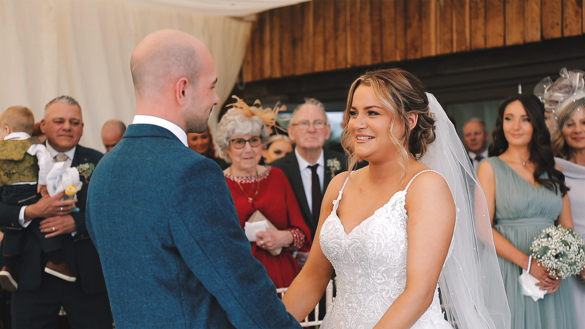 Indoor ceremony at Trevenna in Cornwall with bride in lace gown and groom in blue suit smiling at each other