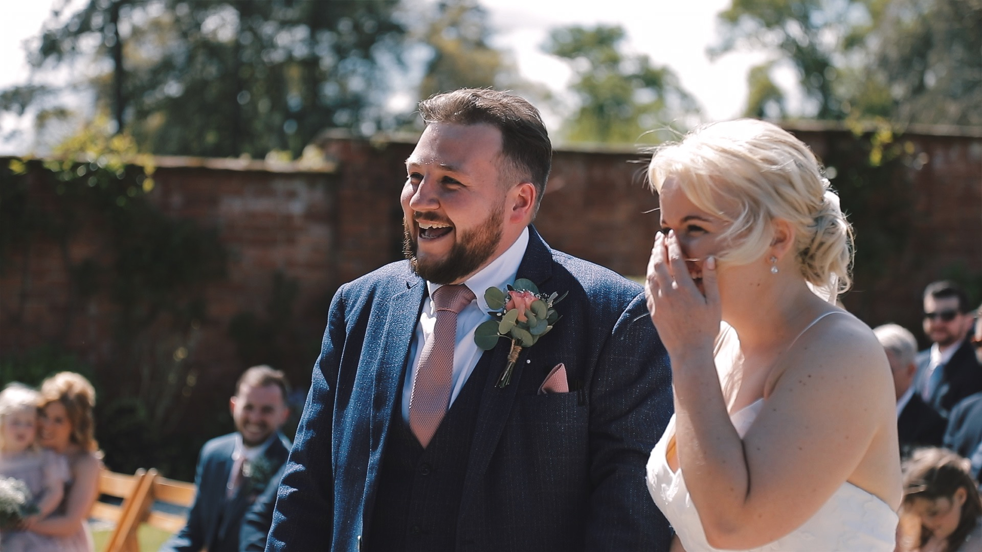 Bride and groom during an outdoor wedding ceremony at Upton Barn and Walled Garden in Devon, smiling and laughing in the sunlit garden surrounded by guests