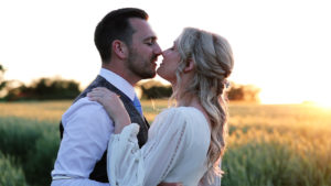 A wedding planning couple kissing in a golden sunlit field at Harefield Barn