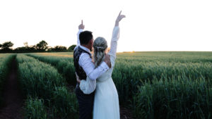A rock'n'roll wedding couple watching the sunset in a field at Harefield Barn after their ceremony readings at their weddding