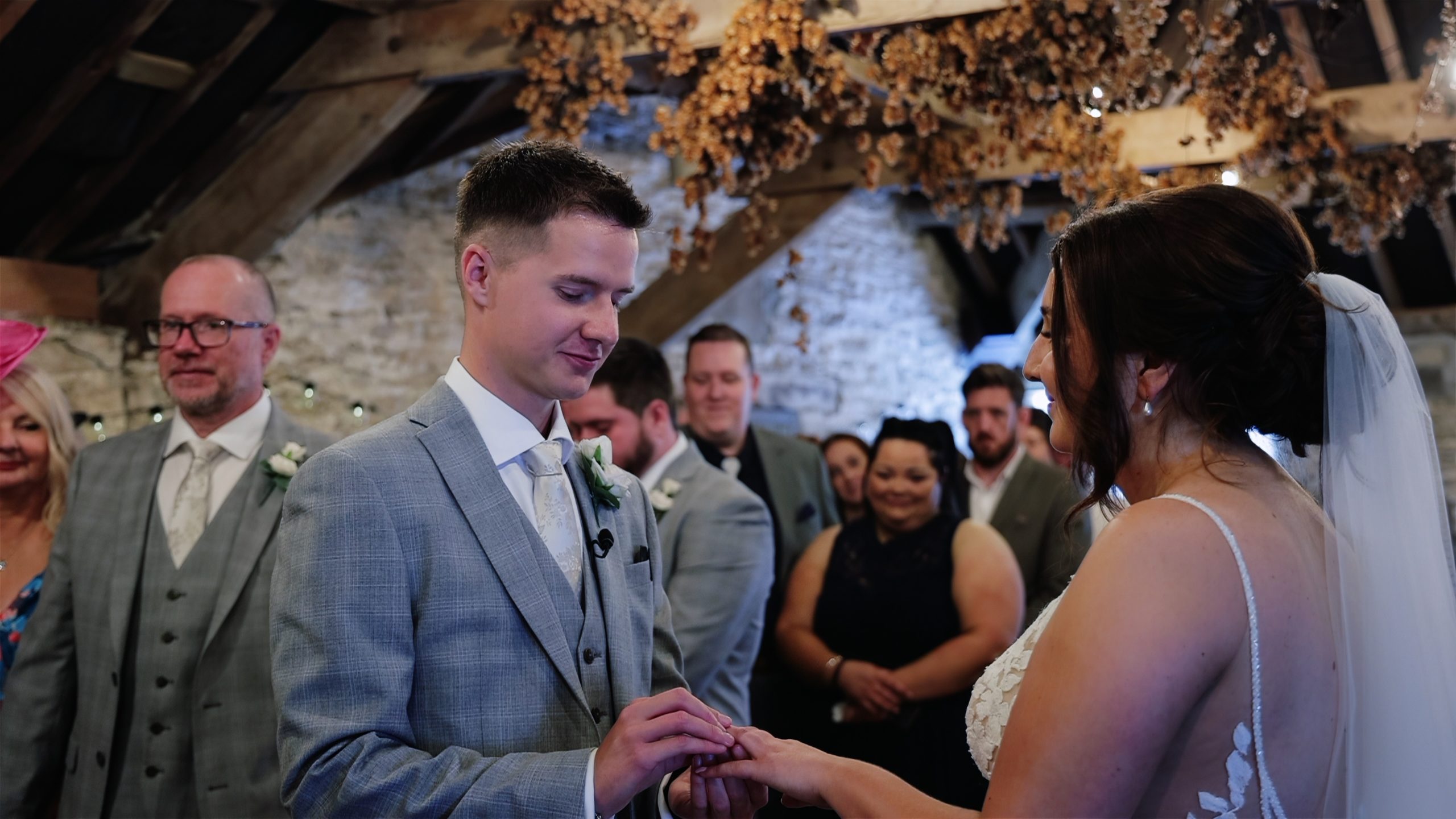 ceremony-readings-for-wedding Bride and groom exchanging rings inside the rustic ceremony barn at Trenderway Farm in Cornwall, smiling as guests watch