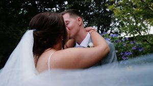 A wedding couple sharing a kiss with the brides veil flowing around them captured by South west wedding videographer