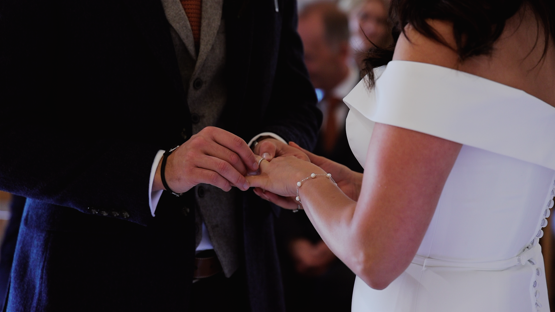 Ring exchange during wedding ceremony inside the barn at Trenderway Farm in Cornwall with bride in an off-shoulder dress