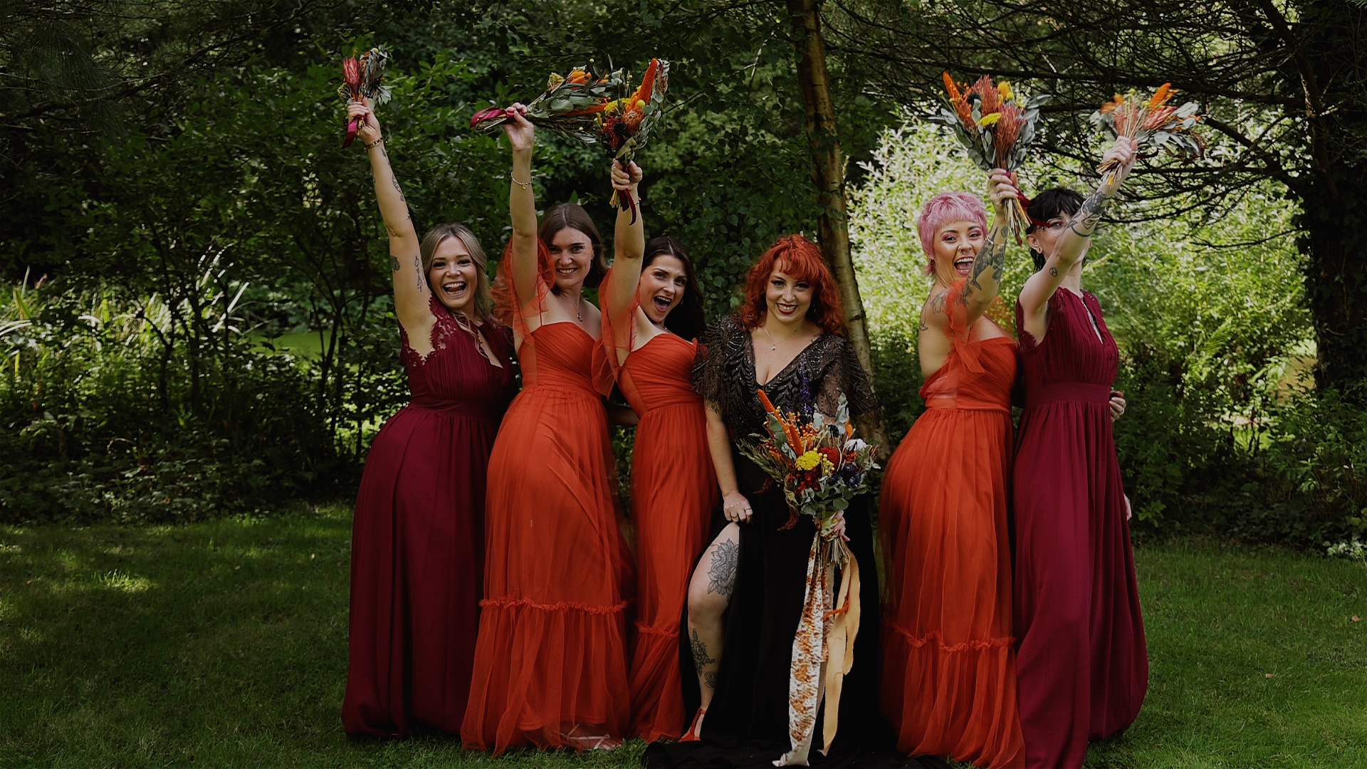A bridal party cheering with their bouquets in the air at Mount Edgcumbe