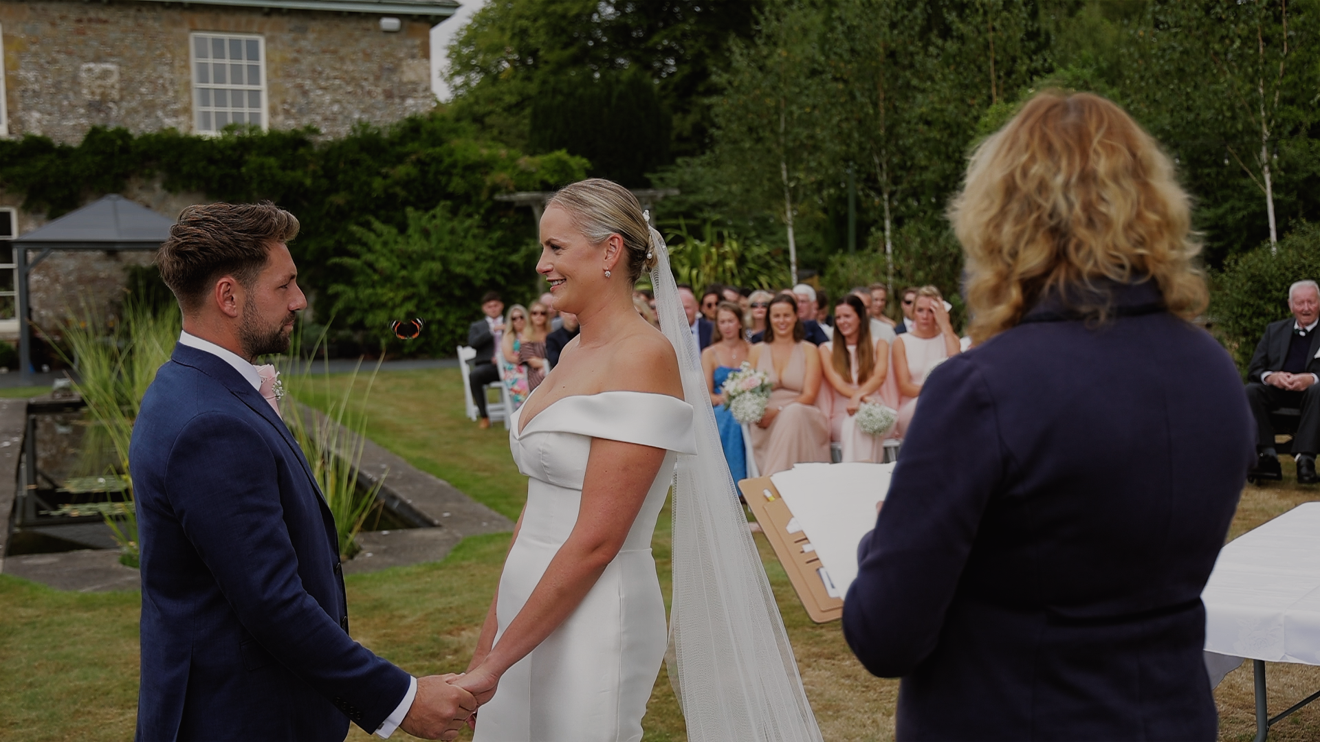 Candid wedding ceremony moment at Glebe Wedding Barn with a butterfly flying between bride and groom as they hold hands