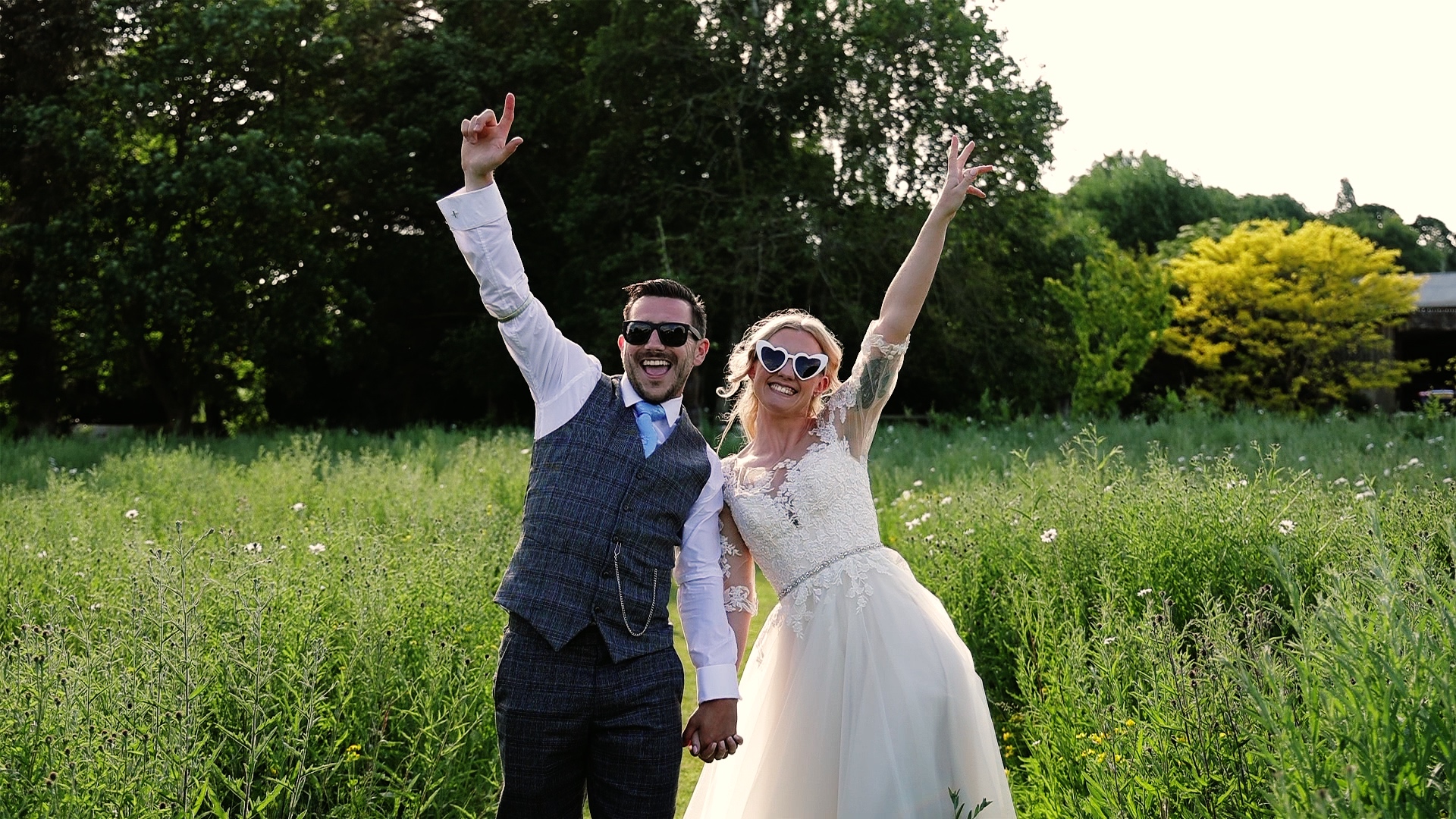 Bride & groom wearing sunglasses punching their air with joy at Harefield Barn