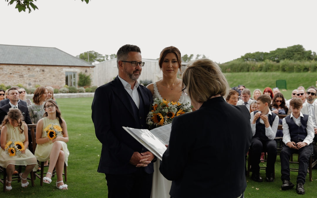 A bride and groom stand in front of the registrar and their wedding guests for the ceremony