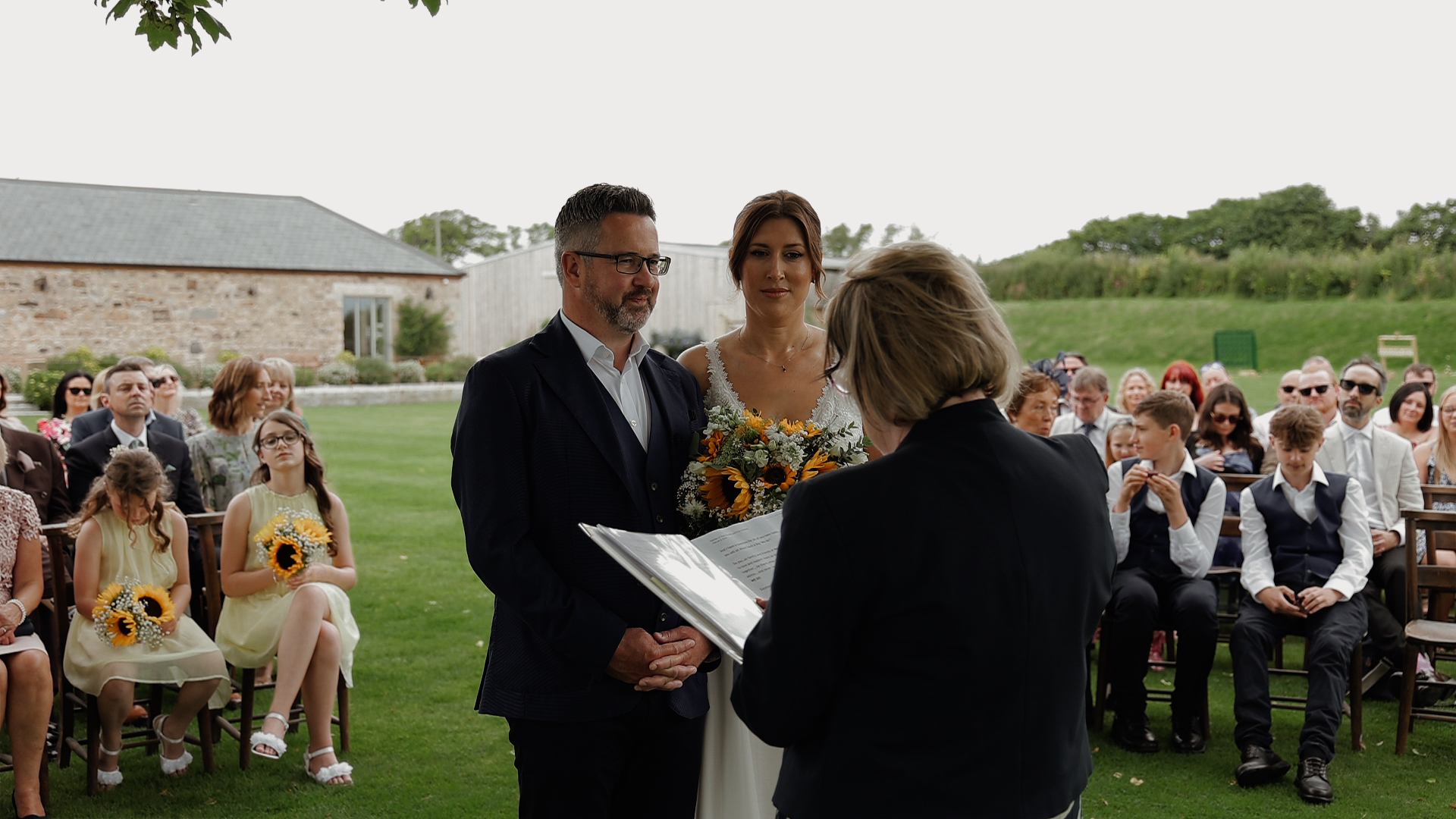 A bride and groom stand in front of the registrar and their wedding guests for the ceremony