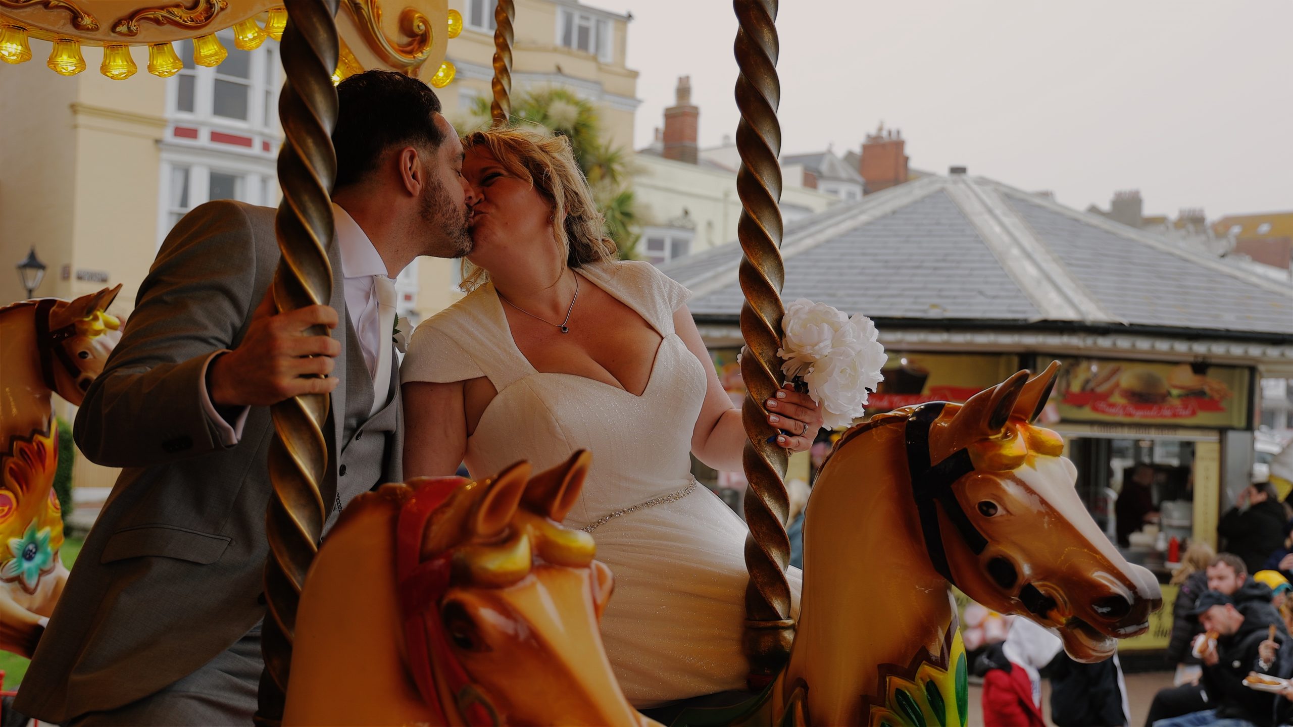 A bride and groom sharing a kiss on a carousel at Weymouth beach