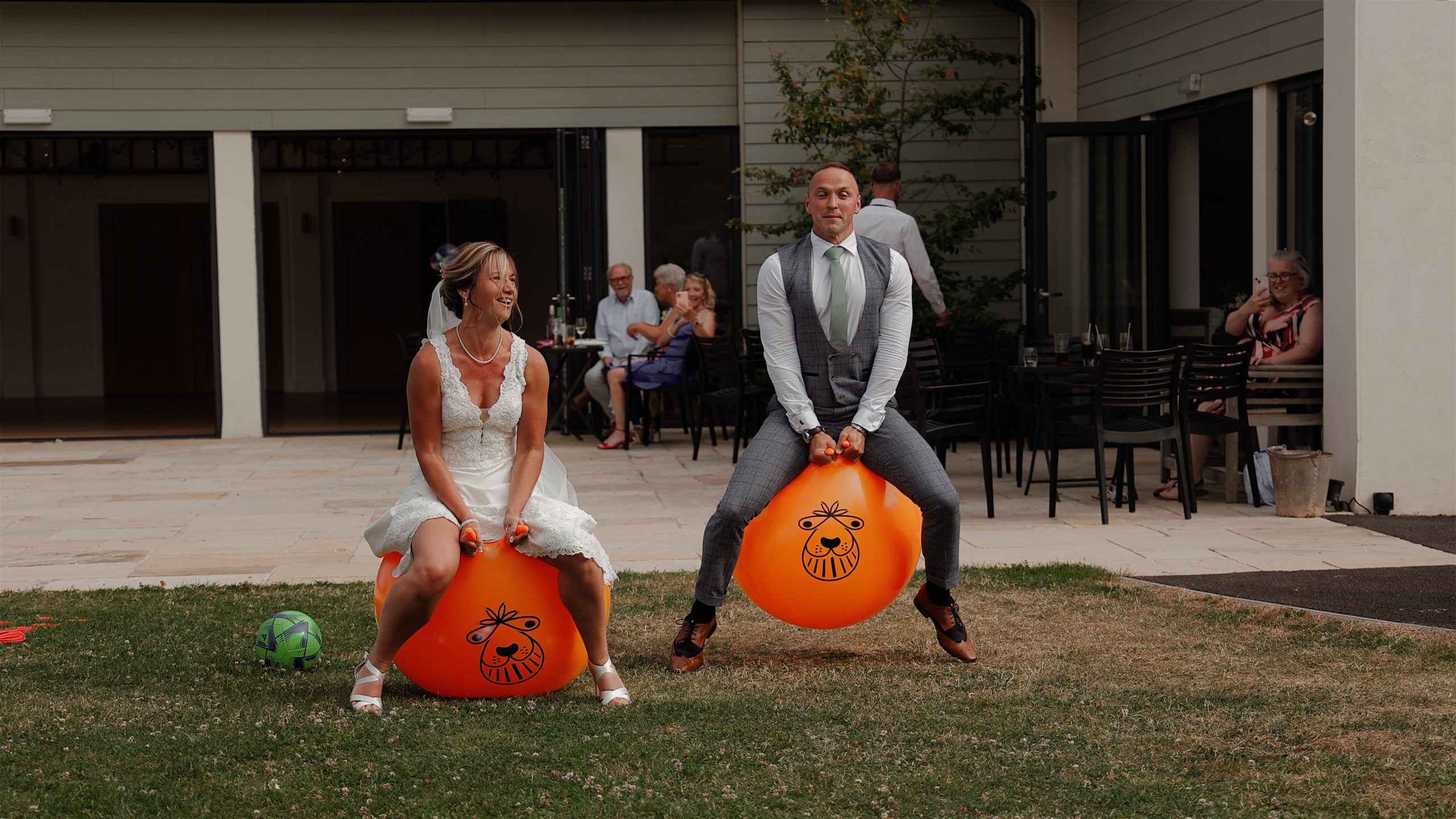 A bride and groom having a race on a pair of orange space hoopers at Harefield Barn