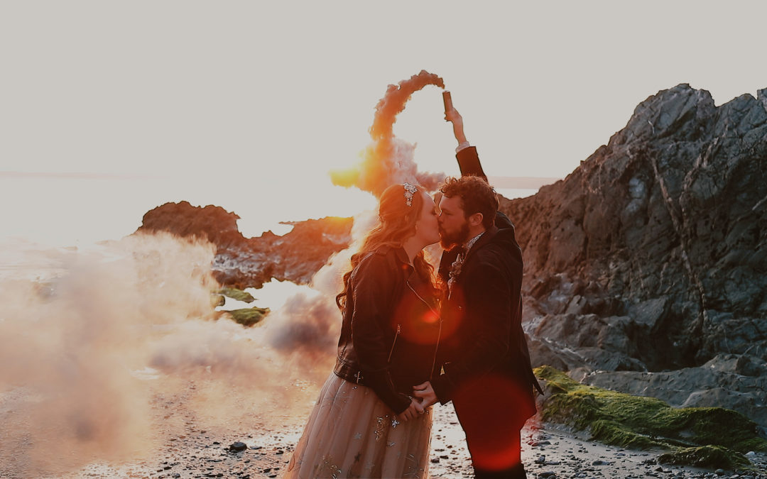 Bride and groom with smoke bombs on a beach at sunset