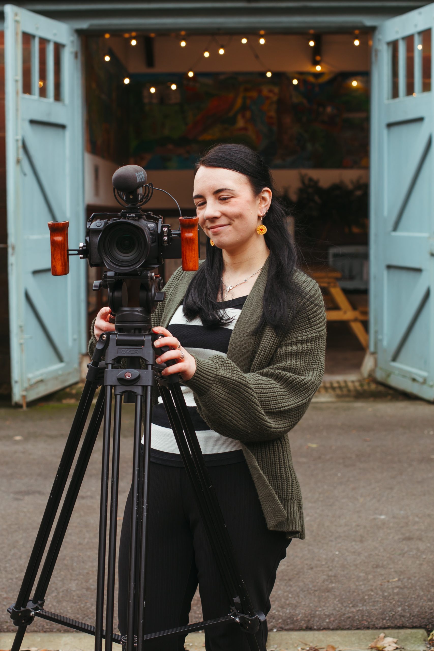 A female wedding videographer smiling at a camera tripod