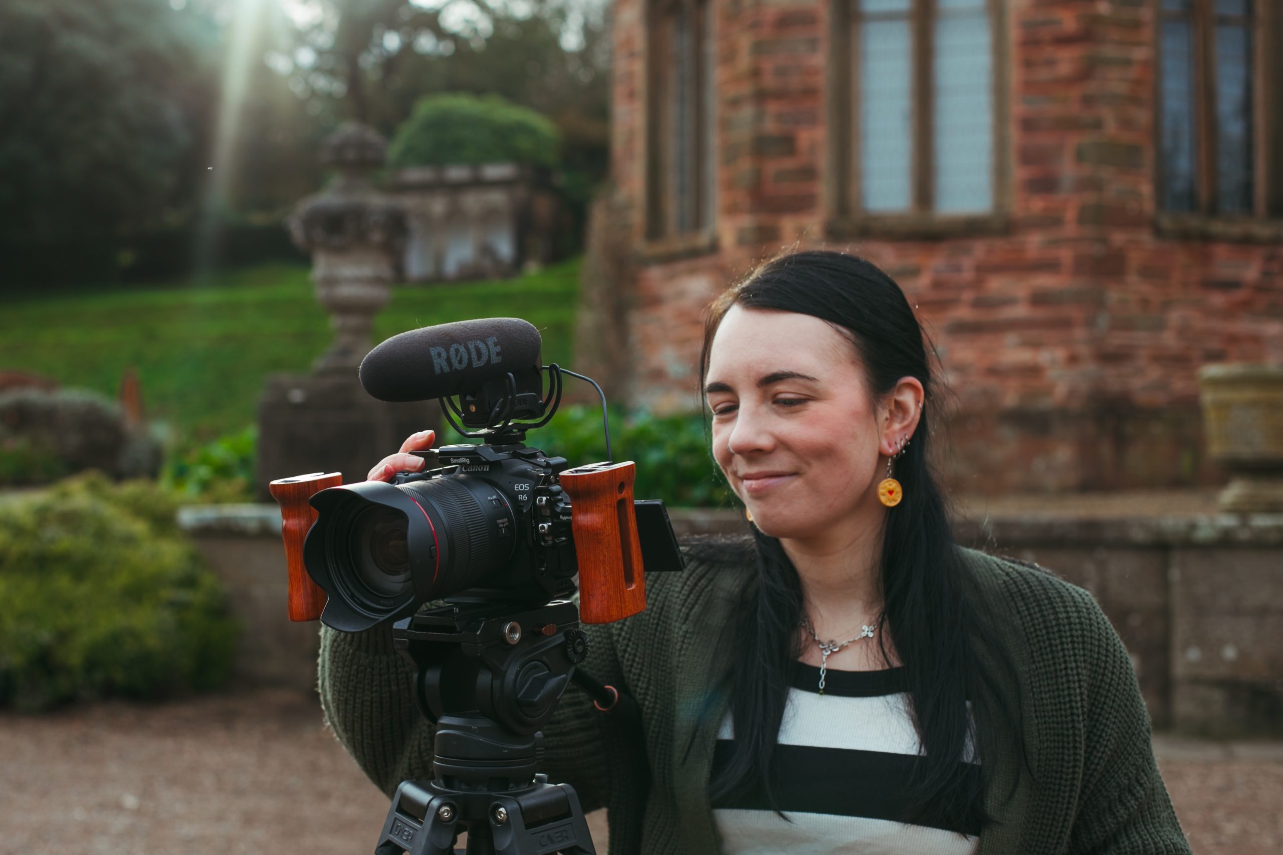 A female wedding videographer smiling at the screen on a camera mounted on a tripod