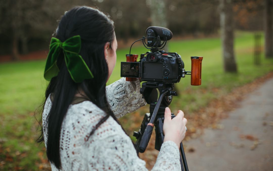 A female wedding videographer standing behind a tripod mounted camera
