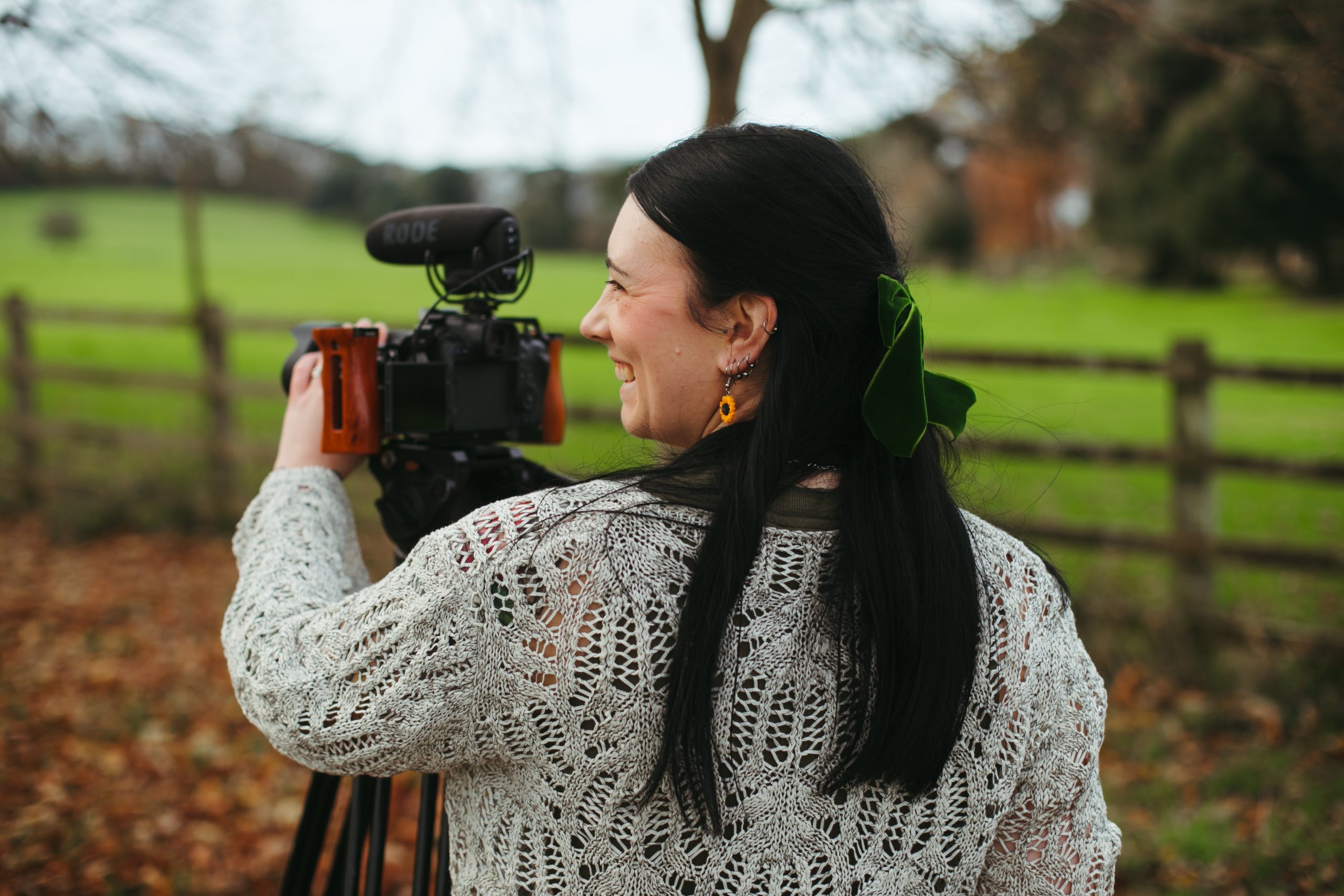 A smiling female wedding videographer standing behind a camera on a tripod