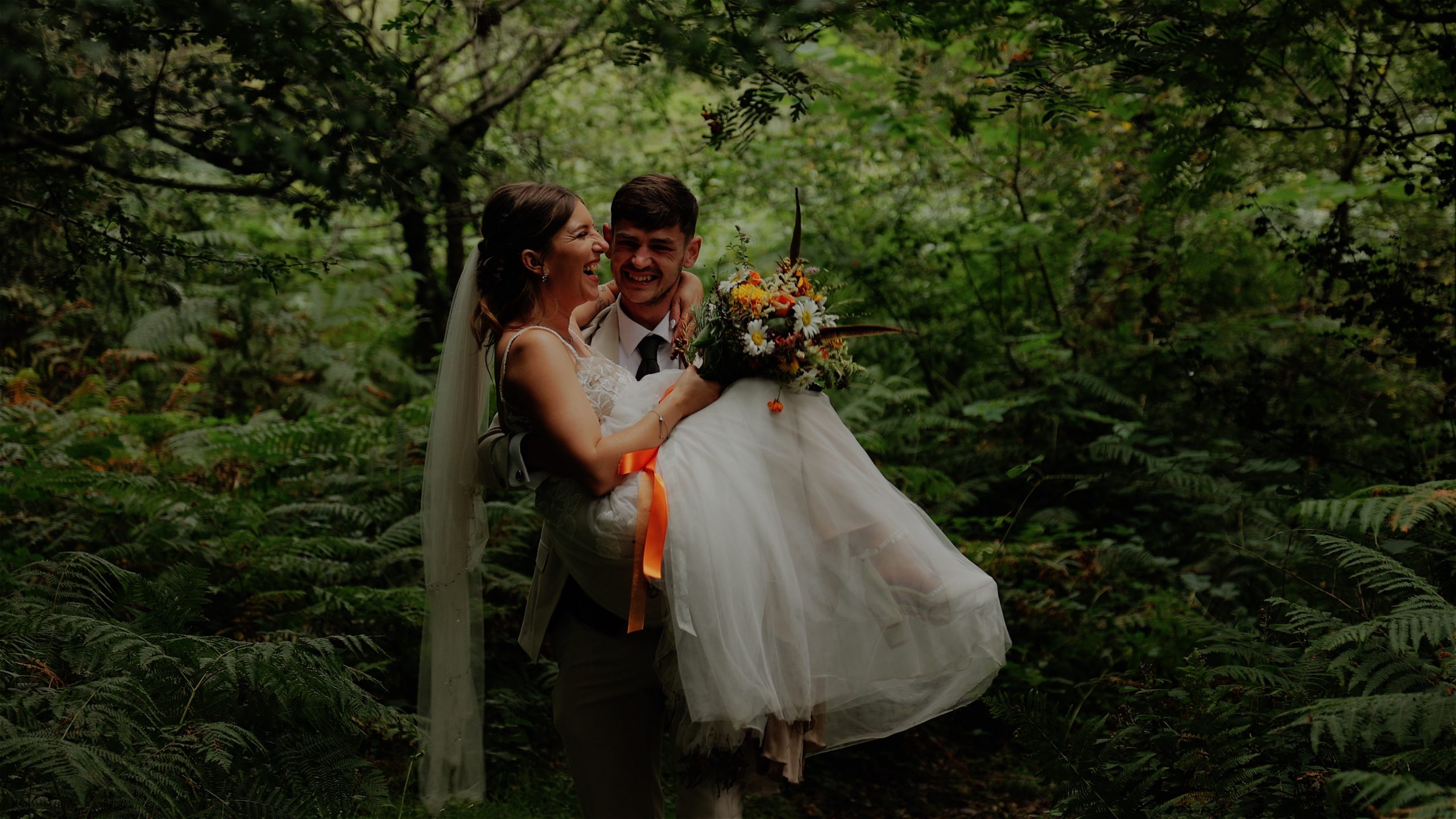 A smiling groom carrying his bride through a forest