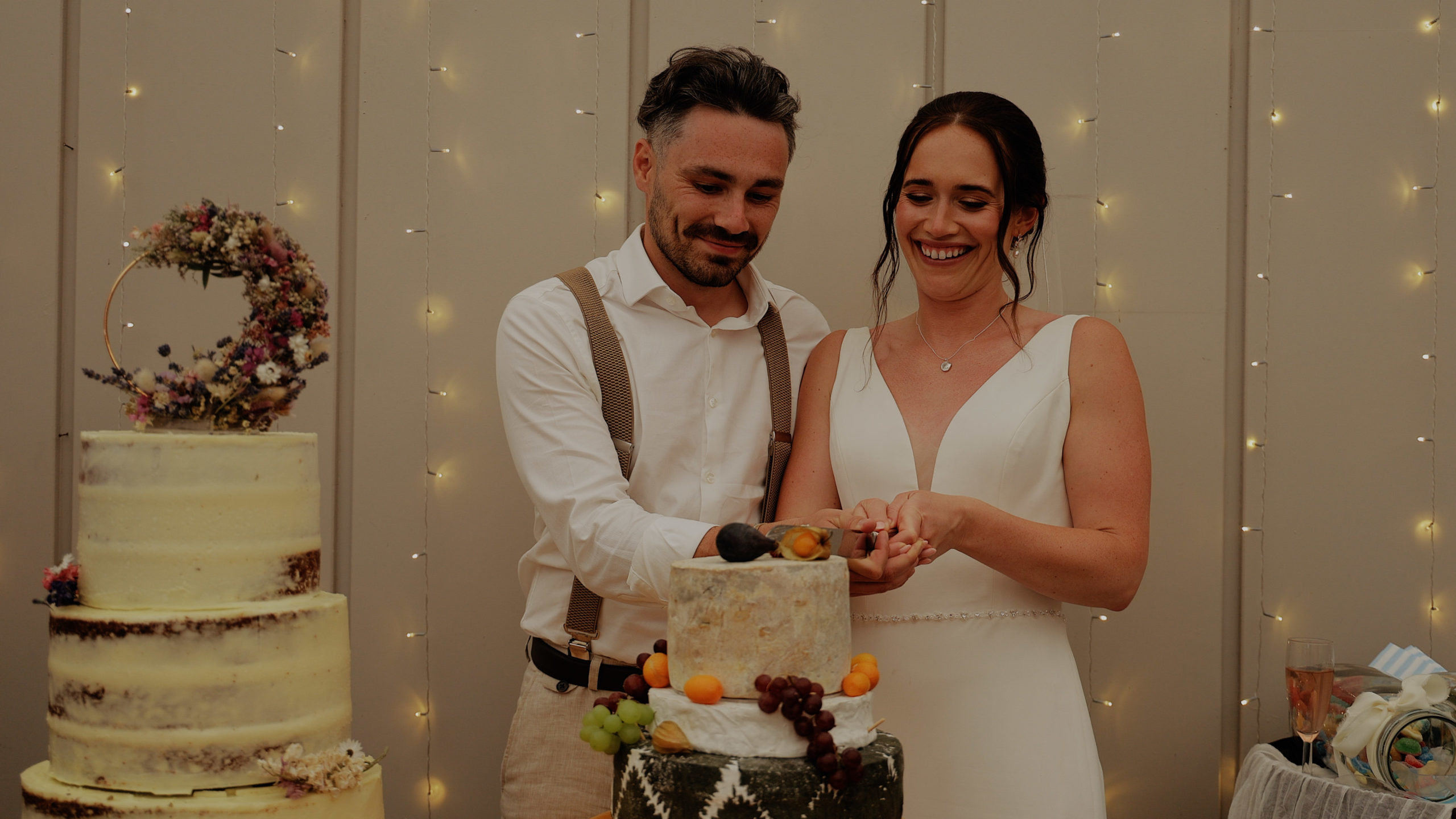 Beth & Kiaran Trevenna cake cut A bride and groom stood in evening sunlight with flowers in the fore ground at Trevenna Barns