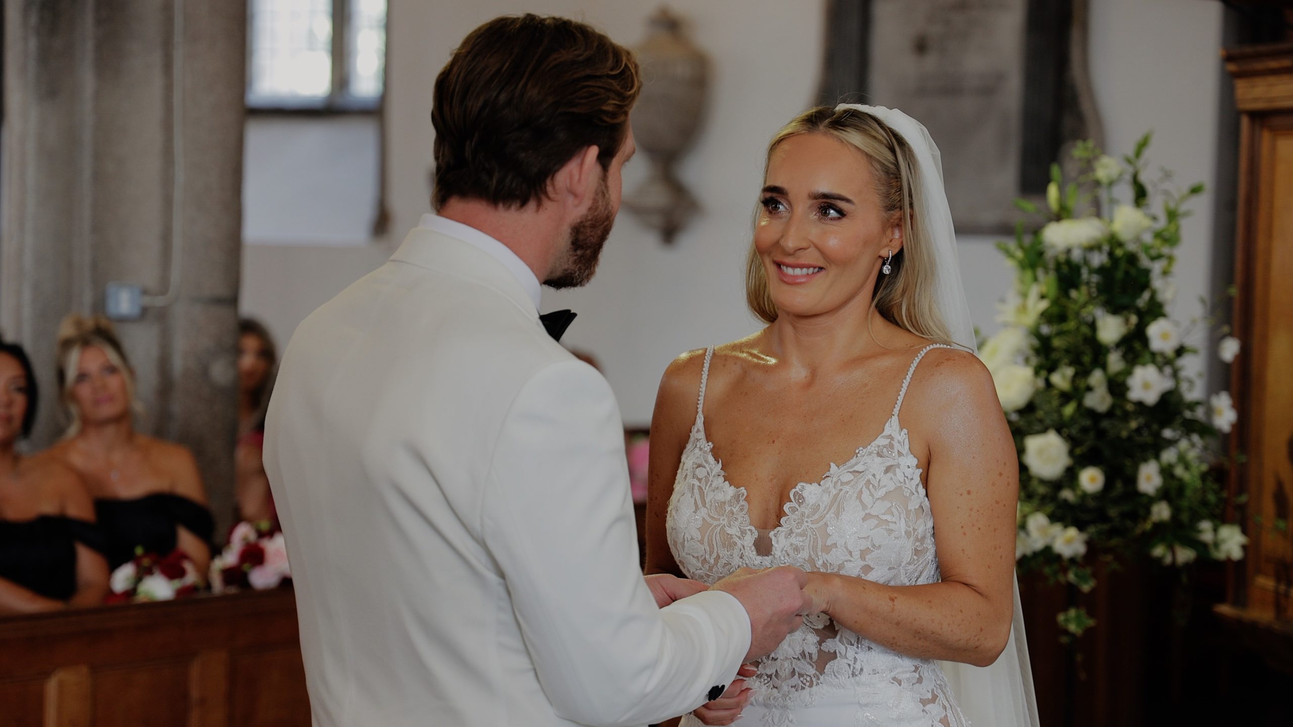 A bride & groom hold each each while their bestman runs around them with a pink smokebomb at Rockbeare Manor
